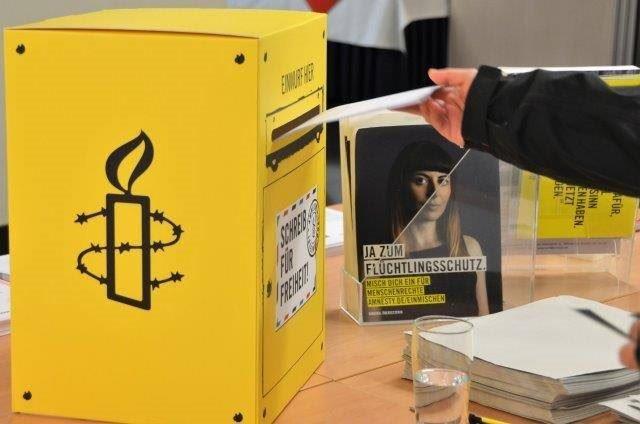 Amnesty-Infotisch mit "Schreib für Freiheit!"-Briefkasten, in den gerade ein Brief eingeworfen wird.