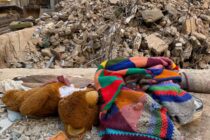 Eine bunte Wolldecke (von der Aachener Strickgruppe) liegt neben einem Teddybär vor den Trümmern eines Hauses in Beirut.