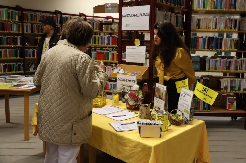 Personen unterhalten sich an einem Amnesty-Infostand in einer Bibliothek.