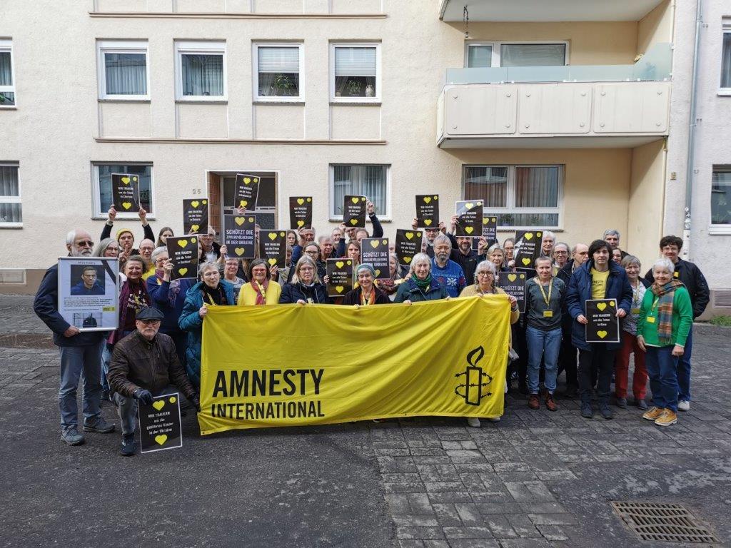 Gruppenfoto der Teilnehmer*innen der Amnesty Regionalkonferenz West in der Bonner Brüdergasse. Sie zeigen Solidaritätsbotschaften für die Ukraine auf Plakaten.