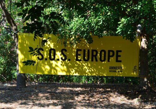 Amnesty International Banner aufgespannt im Schatten unter Bäumen mit der Aufschrift "S.O.S. Europe"