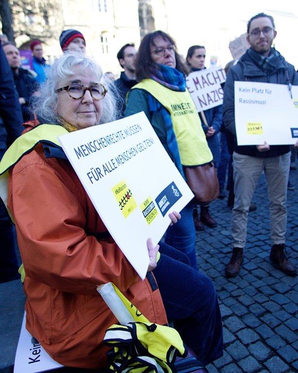 Menschen mit Amnesty-Leibchen bei einer Demo auf dem Aachener Katschhof halten Schilder mit den Aufschriften "Manschenrechte müssen für alle Menschen gelten" und "Kein Platz für Rassismus".